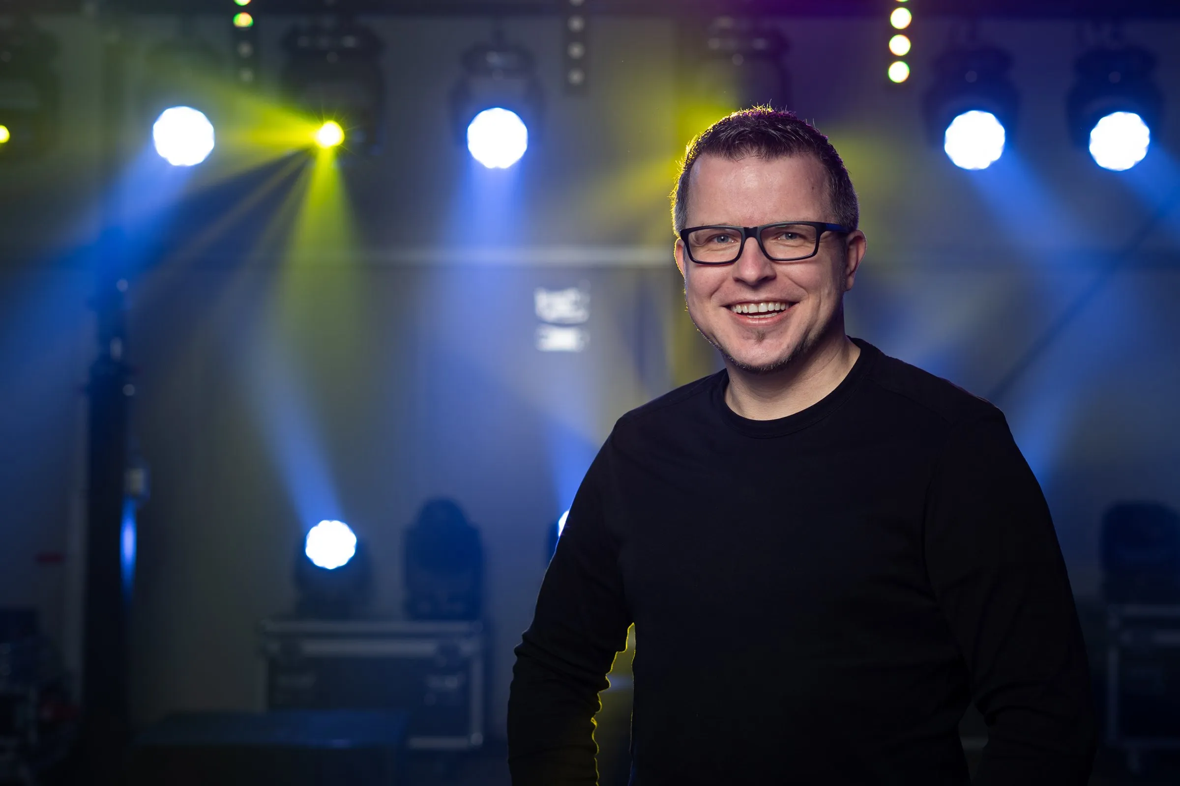 DJ Matthias Steenblock lächelnd vor einer Lichtshow